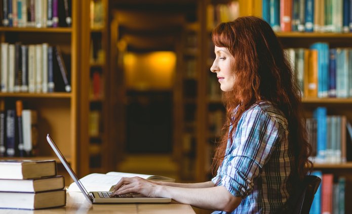 kolorowe zdjęcie przedstawia młodą studentkę pracującą w bibliotece