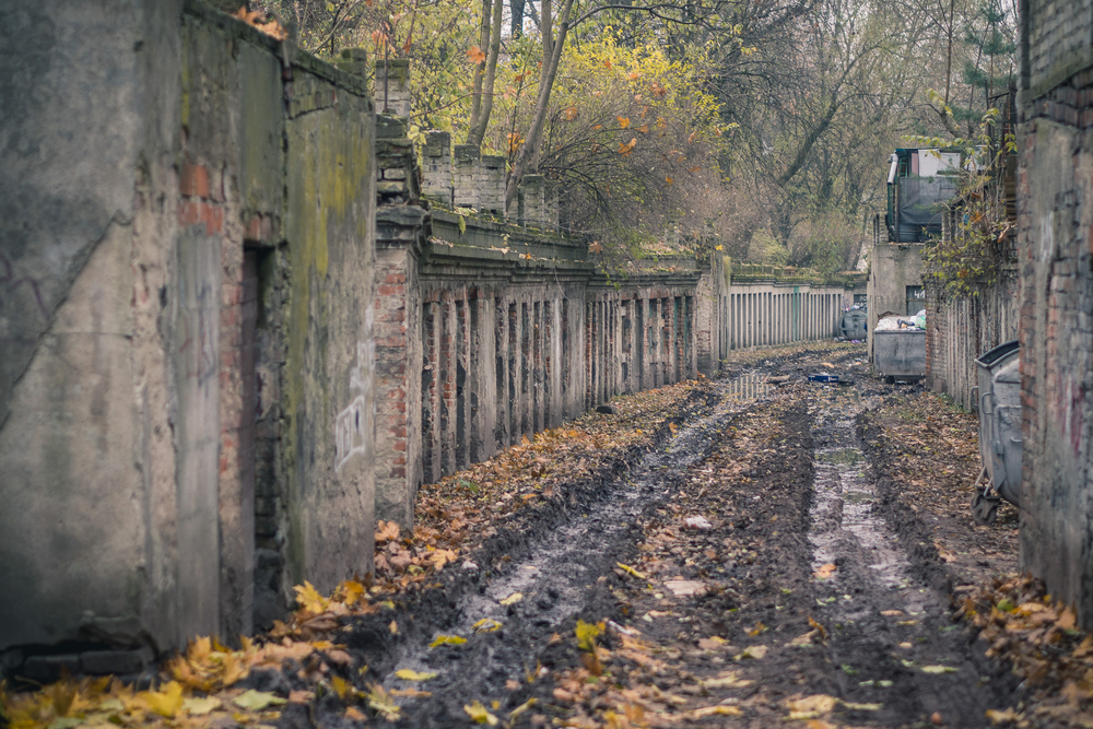 zdjęcie pokazuje błotnistą drogę, która wiedzie między rzędami komórek znajdujących się w starych, jednokondygnacyjnych budynkach zdjęcie pokazuje błotnistą drogę, która wiedzie między rzędami komórek znajdujących się w starych, jednokondygnacyjnych budynkach