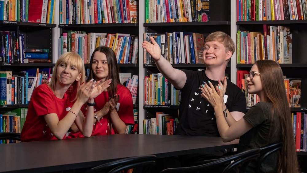 grupa studentów siedzi przy stole w bibliotece i dyskutuje 