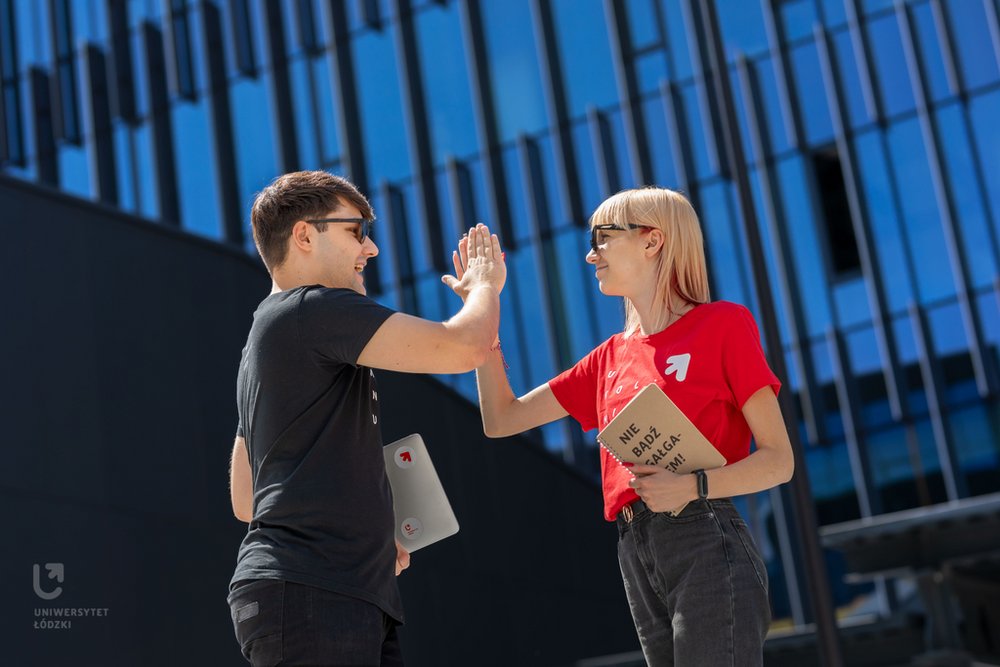 Młoda kobieta z notesem w dłoni i mężczyzna z komputerem w dłoni przybijają sobie piatkę