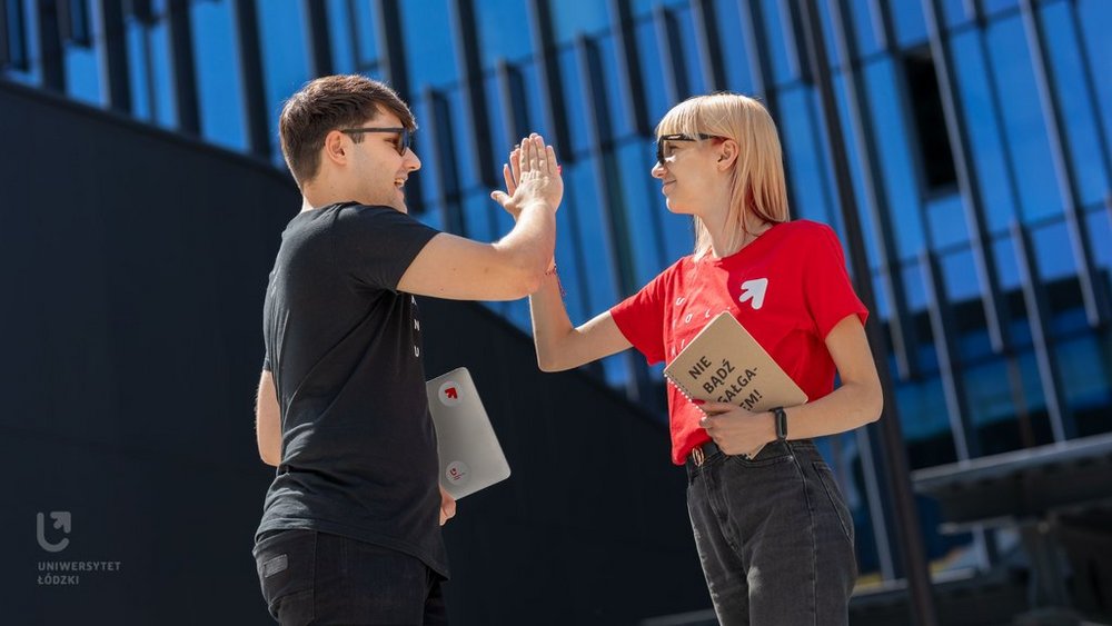 Dwoje młodych ludzi, dziewczyna i chłopak, stoją na dworze w słoneczny dzień i przybijają sobie piątkę