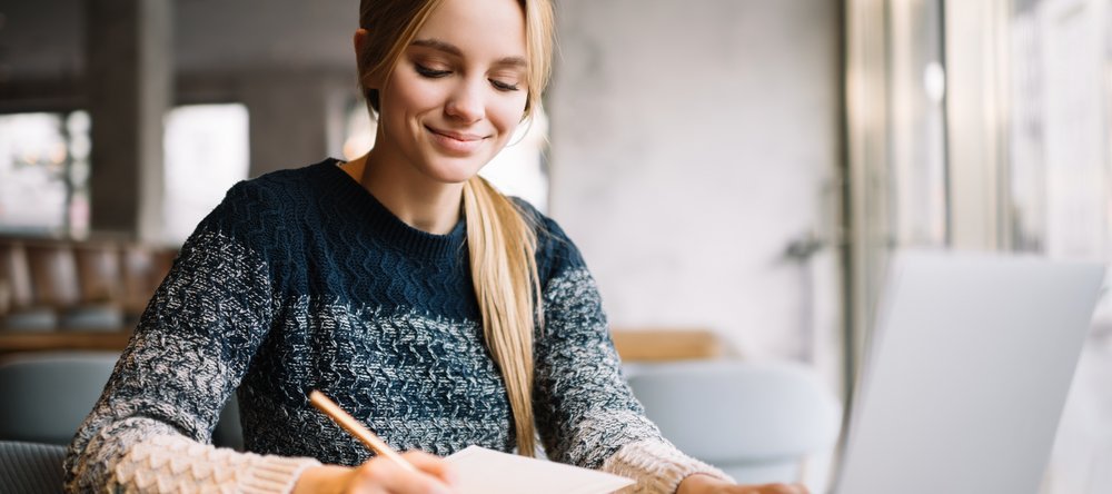 Kobieta w granatowym swetrze robiąca notatatki