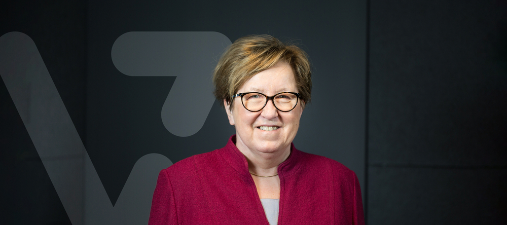 prof. Bryszewska na ciemnym tle, obok grafika w kształcie litery V