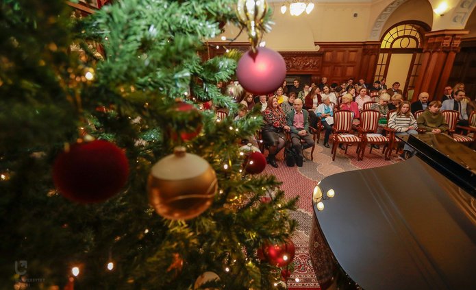 Zdjęcie przedstawia salę w pałacu Biedermanna podczas koncertu. Widać fragment choinki, fortepianu oraz grupę osób siedzących na krzesłach.