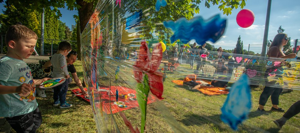Dzieci malujące na folii rozwieszonej pomiędzy drzewami