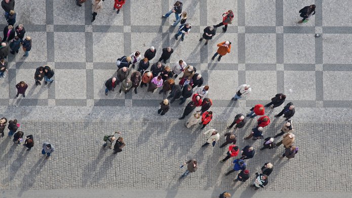 Na zdjęciu widać grupę ludzi. Widziani są z góry, z lotu ptaka. Stoją w kilku miejscach na chodniku lub kamiennych płytach.
