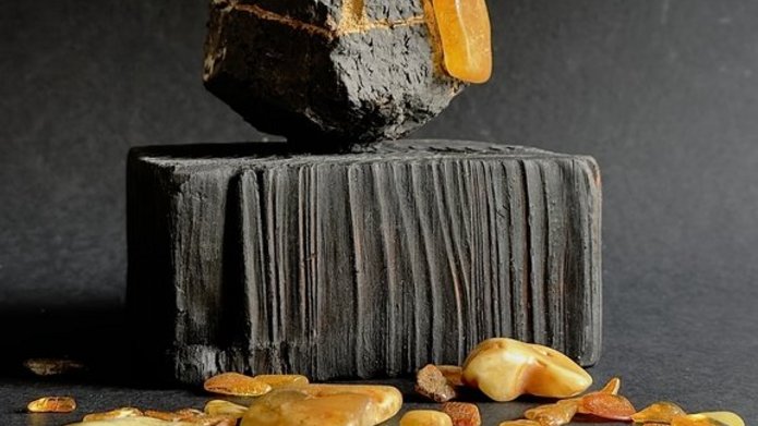 Na zdjęciu widać rozsypane bursztyny oraz kamień lub ceramikę w kształcie sześcianu w kolorze czarnym.