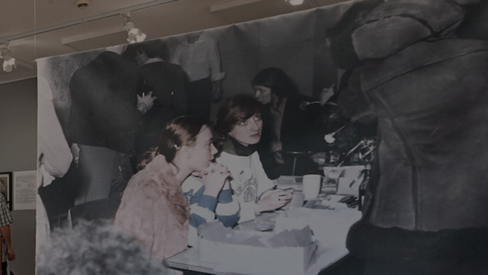 Na obrazku widać zdjęcie kobiet. Jest to fragment pracy artystycznej - wydruk zdjęcia na tkaninie wisi na żyłkach. Widoczne na nim są młode kobiety siedzące i rozmawiające ze sobą. Są to strajkujące studentki Uniwersytetu Łódzkiego. Strajk odbył się w 1981 roku.