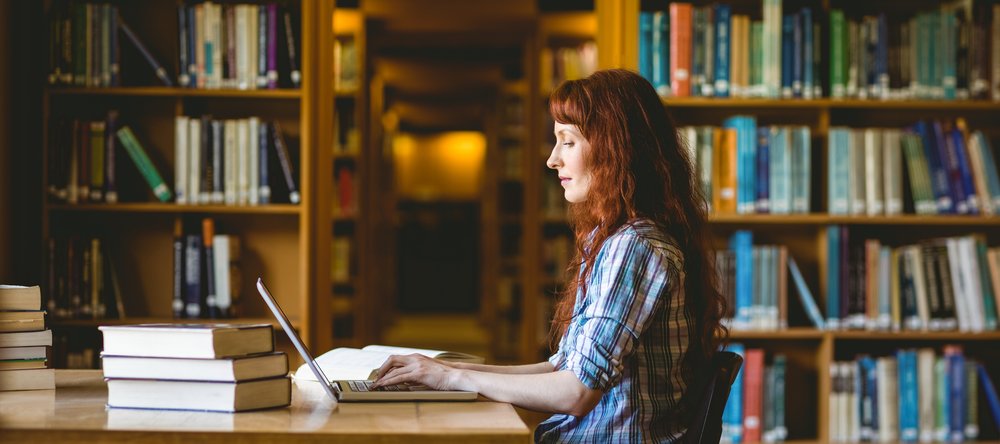 kolorowe zdjęcie przedstawiające studentkę pracującą w bibliotece; zdjęcie promuje artykuł poświęcony nowym zasadom konkursu Studenckie Granty Badawcze 2023