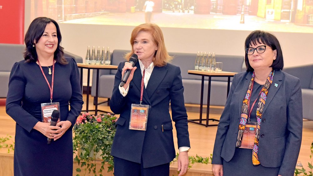trzy kobiety stoją w auli i przemawiają