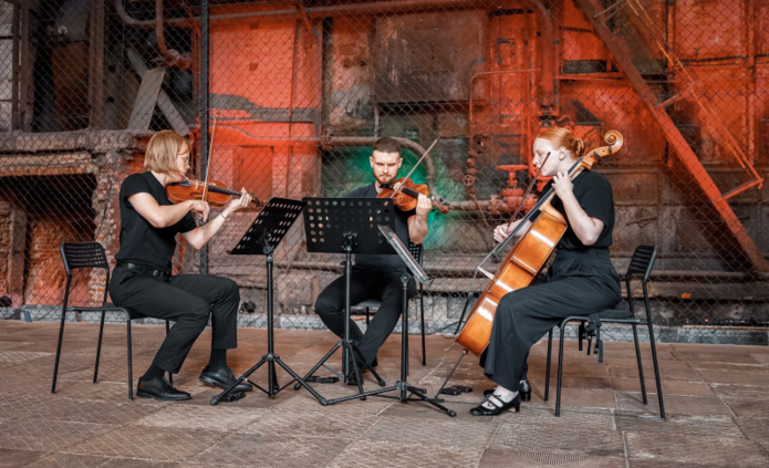 The photo shows three people playing string instruments
