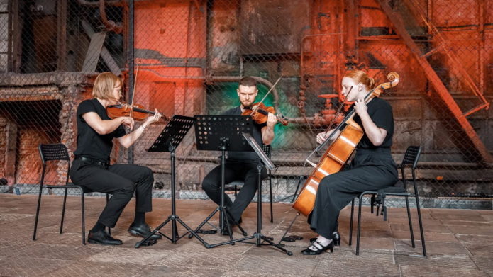 Na zdjęciu widać trójkę osób grających na instrumentach smyczkowych.