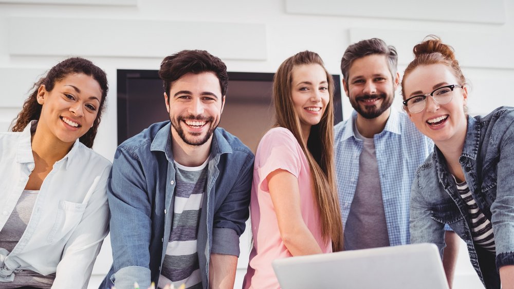 Grupa uśmiechniętych ludzi stojących obok stołu, na którym leży laptop