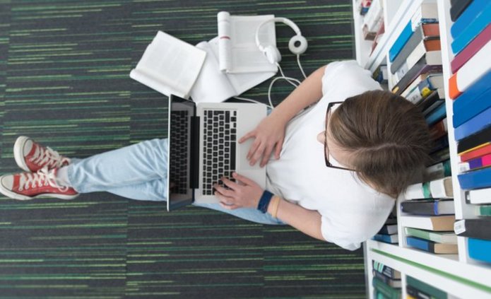Osoba studiująca siedząca w bibliotece z komputerem