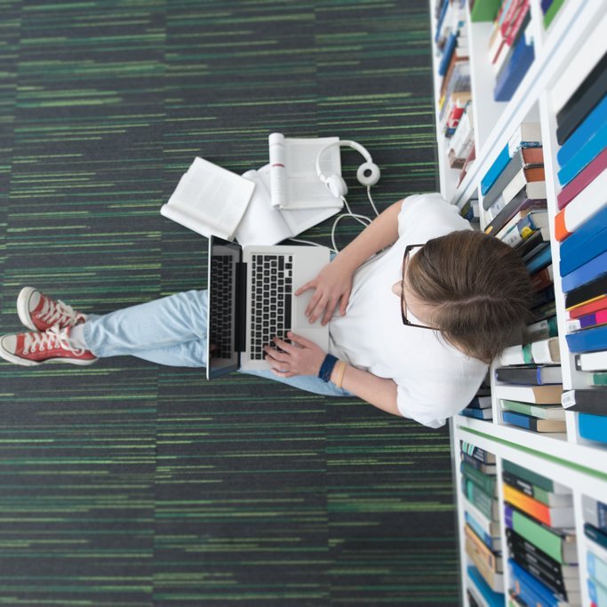 Osoba studiująca siedząca w bibliotece z komputerem