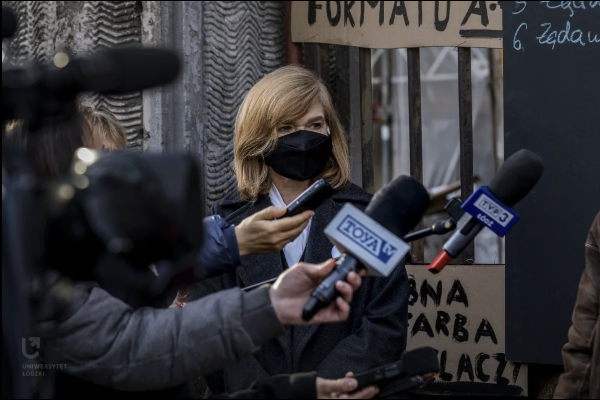Portret rektor Żądzińskiej w maseczce, na konferencji prasowej, na tle transparentów