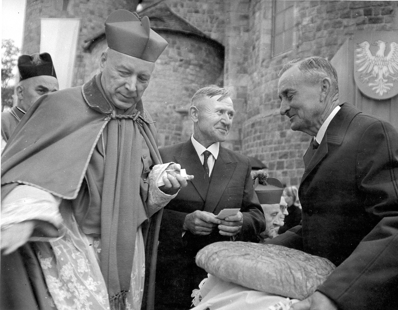 Zdjęcie archiwalne, fragment mszy. Kardynał Wyszyński w pierwszym planie, obok dwóch starszych mężczyzn.