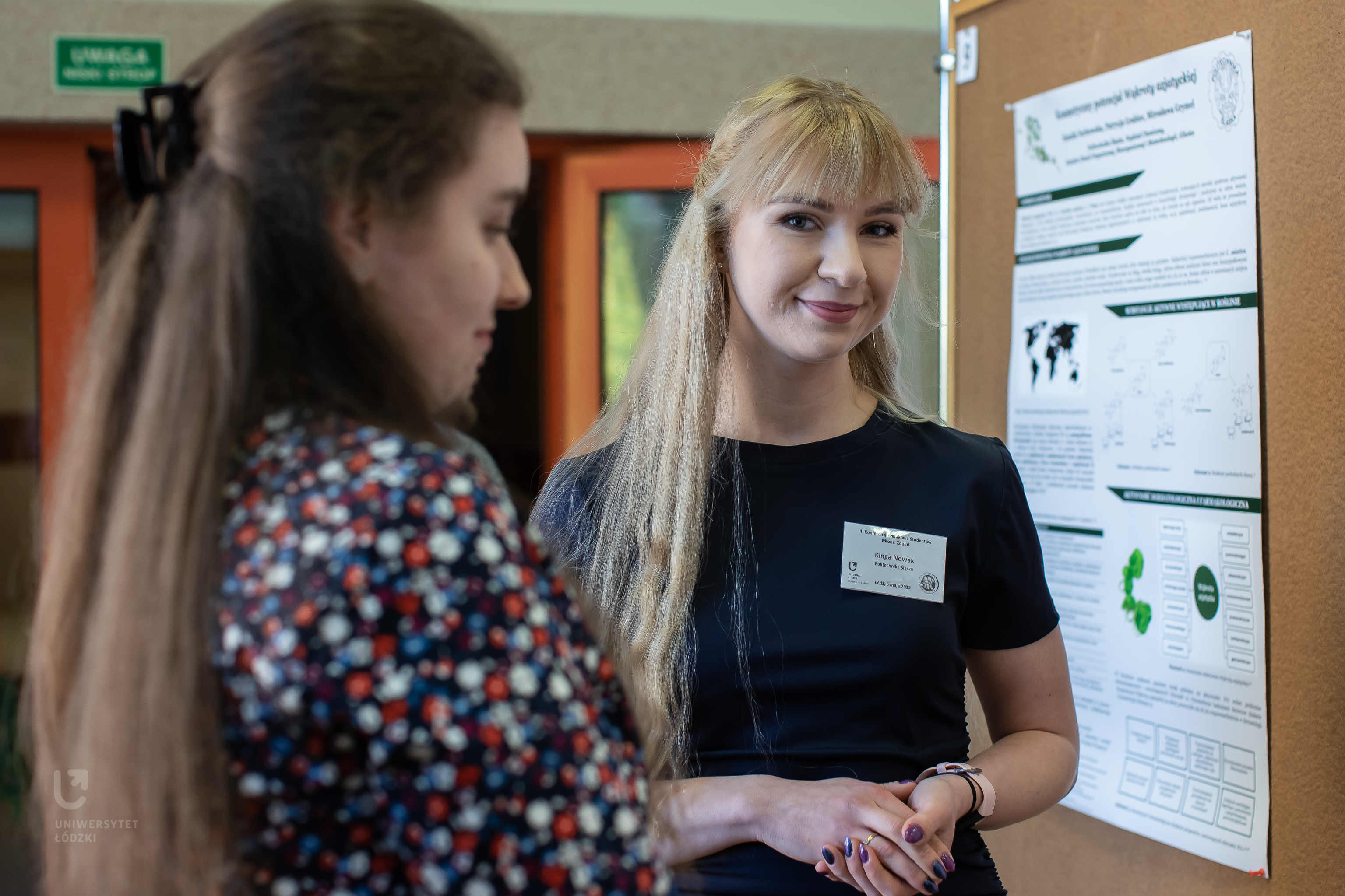 Dwie młode kobiety stojące przy tablicy z plakatem