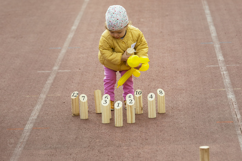 Dziecko z żółtym balonem, stojące wśród drewnianych zabawek