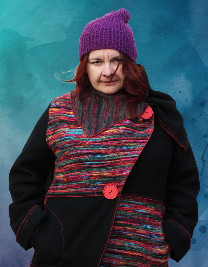 portret laureatki w płaszczu z kolorowymi akcentami w fioletowej czapce podkreślającej rudy kolor włosów